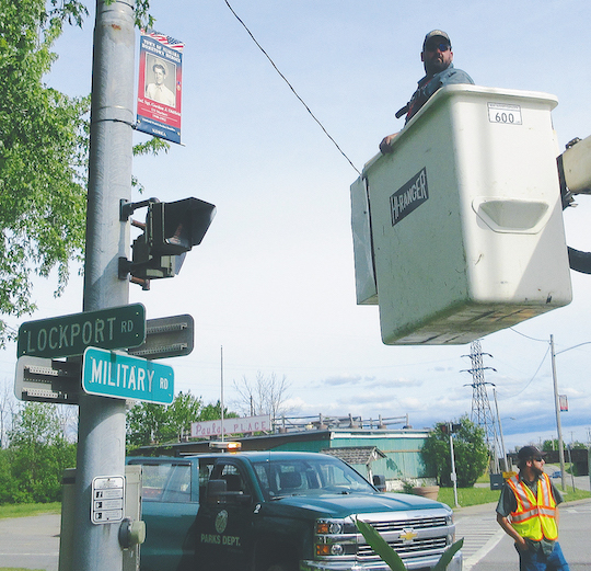 Town of Niagara Parks Department employees Phil Mitchel (bucket operator) and Vince Zuccari (road safety coordinator) work on mounting a banner at the corner of Lockport and Military roads. (Submitted photo)